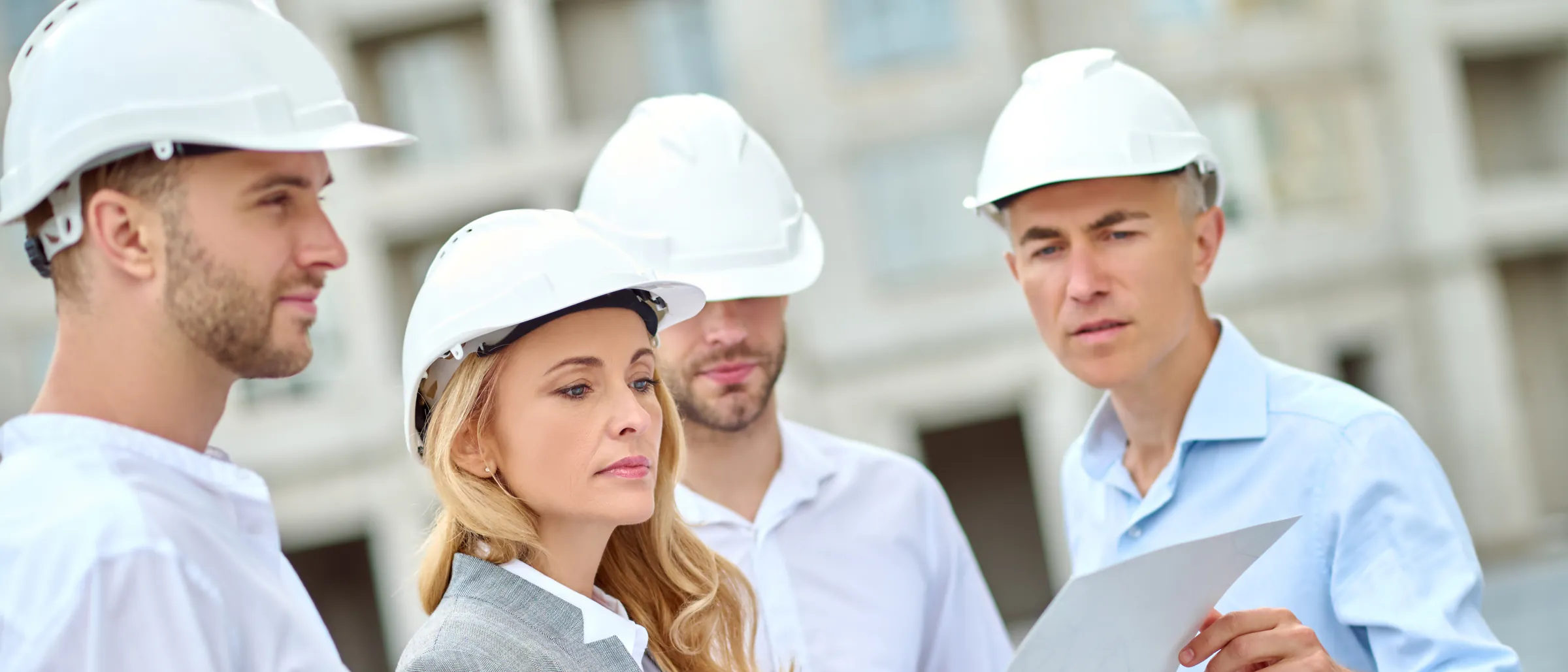 Four engineers in white hard hats reviewing drawings together on a construction site