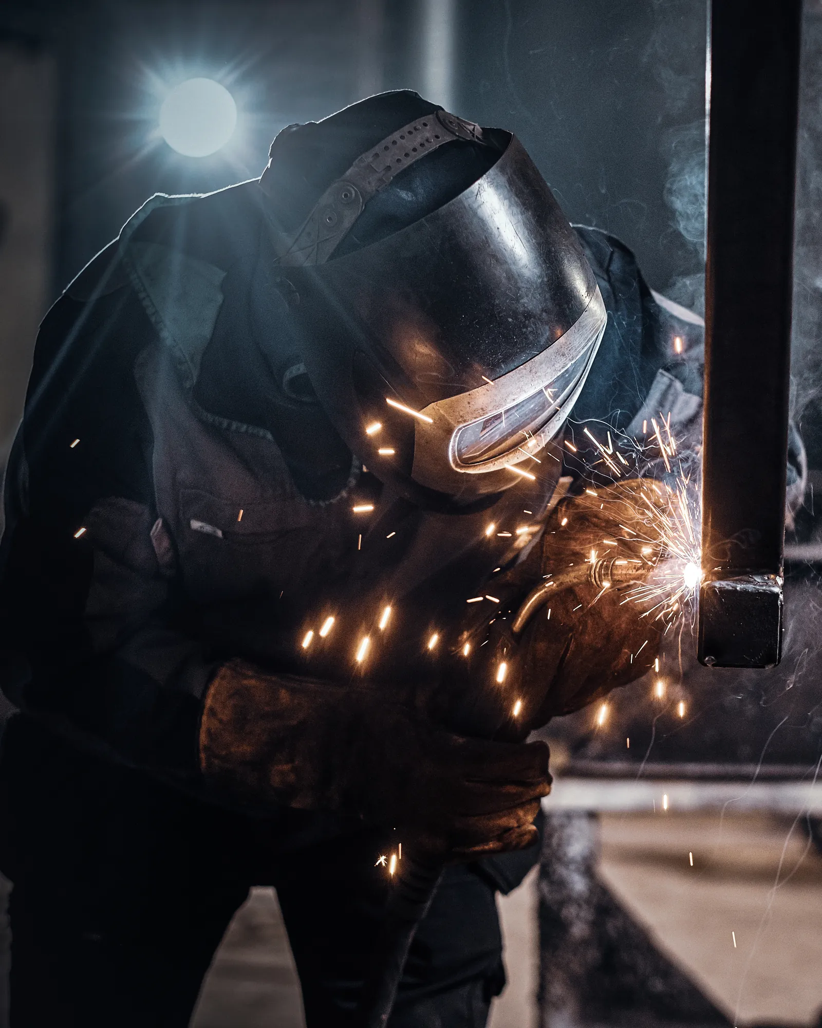 A welder in a protective helmet joining steel, with sparks flying