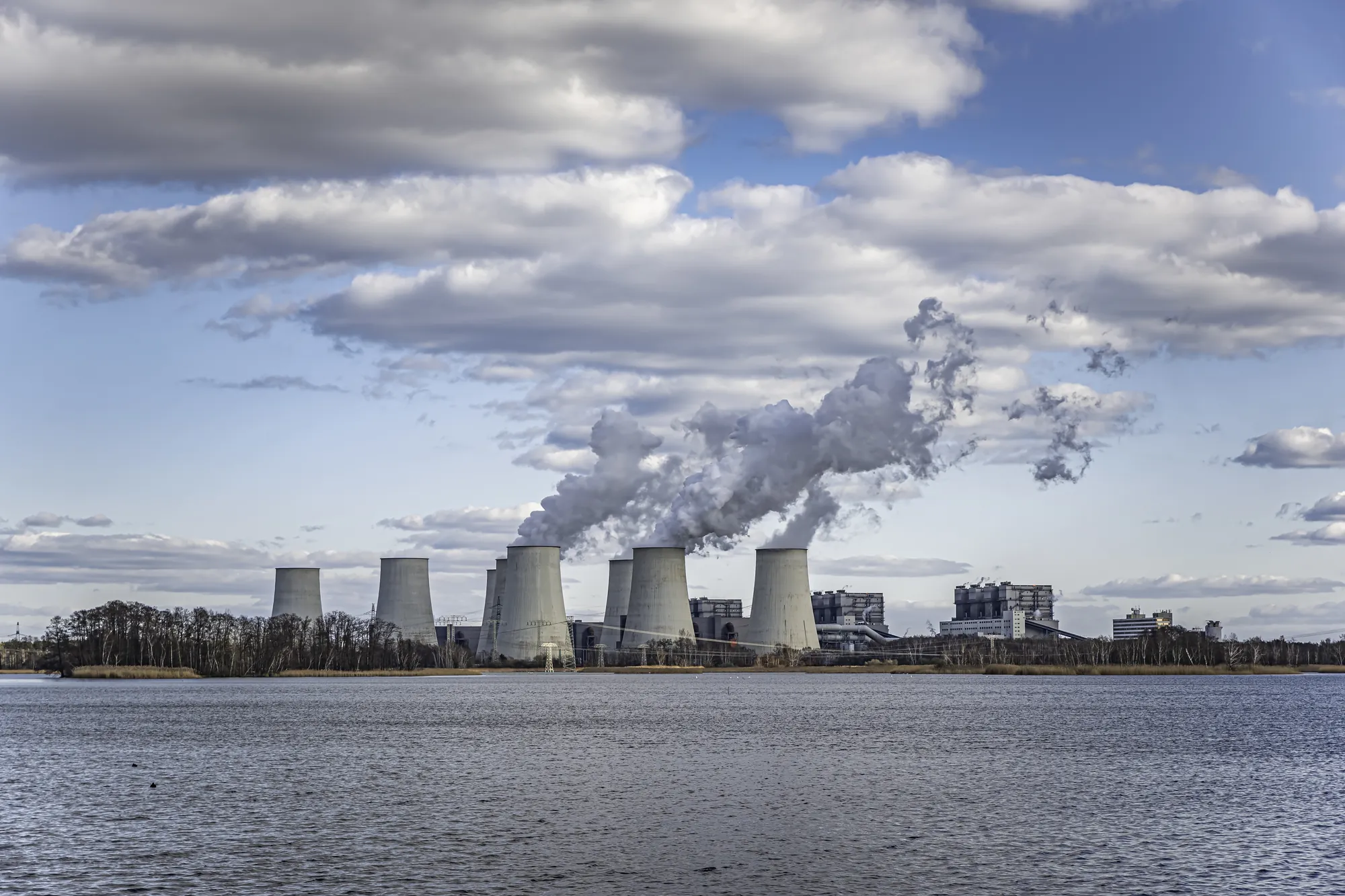 Cooling towers releasing steam beside a lake under a cloudy sky, illustrating a former coal-fired power site