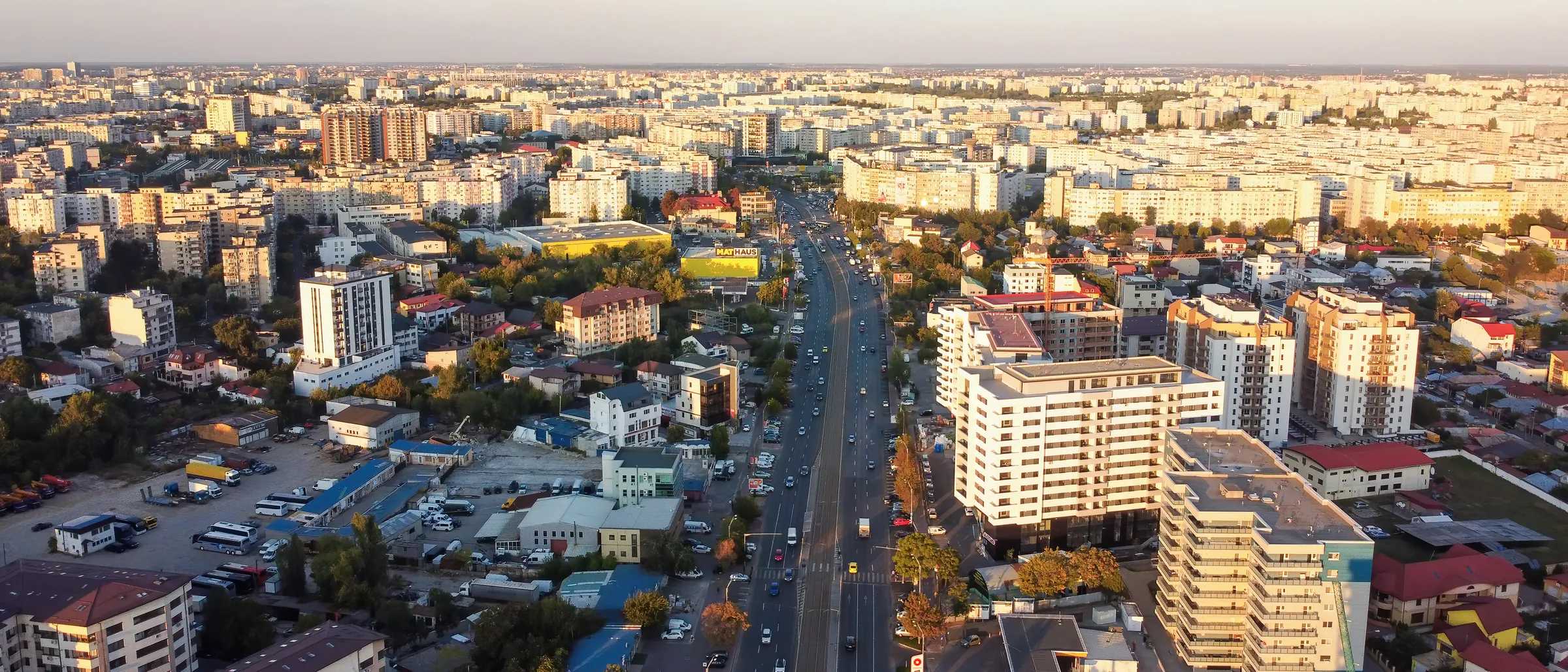 Aerial view of Bucharest at golden hour, with a wide boulevard running between residential and office buildings